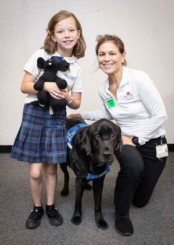 Patient Niah Carver with facility dog Squid and his handler, Leslie Grissim, MA, CCLS. (photo by Erin O. Smith)