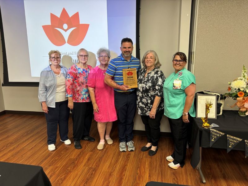 Six hospital team members pose together, with one holding a Patient and Family Choice Award plaque, in front of a presentation screen and decorated award table.