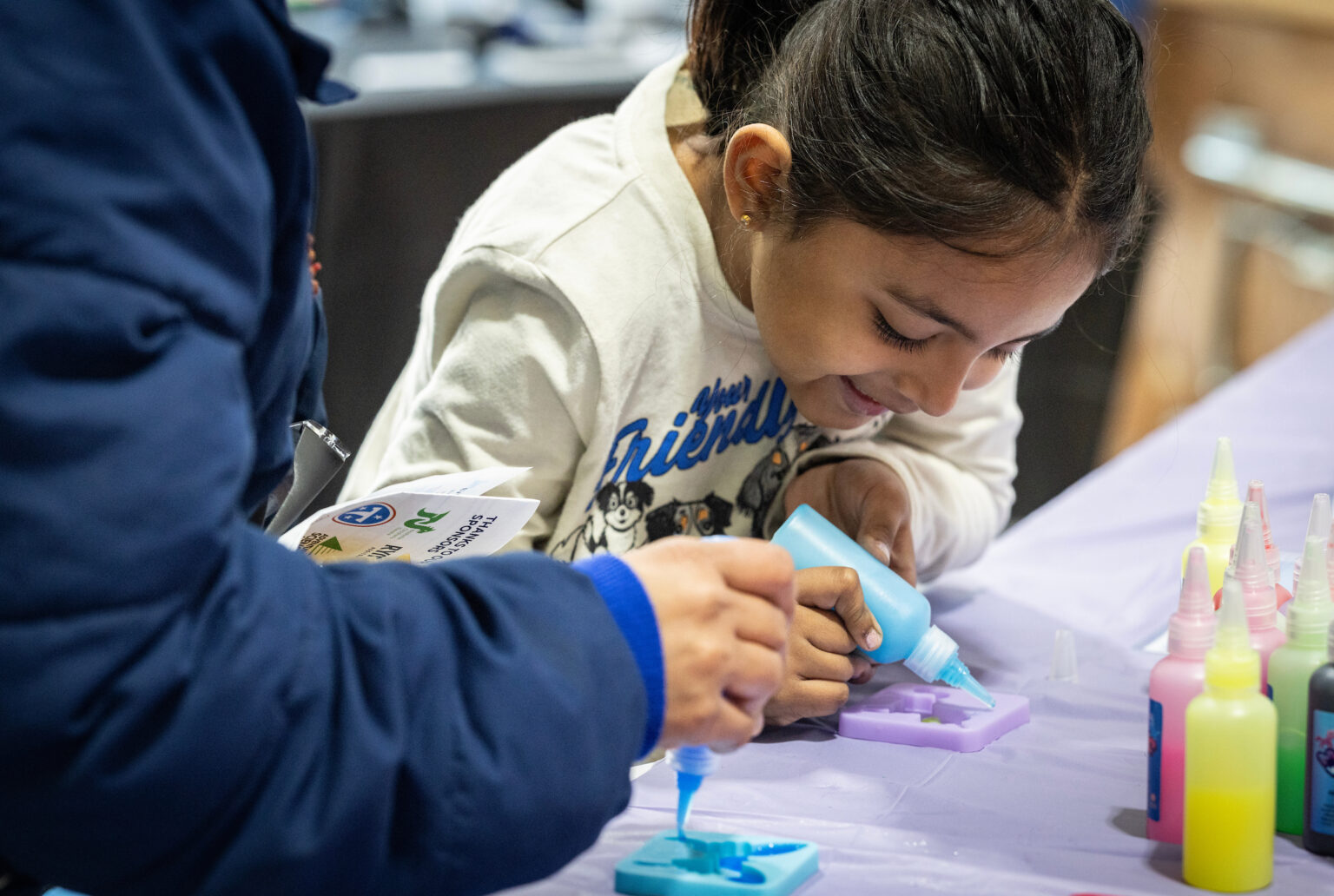 Nyasa Patel, 6, mixes colorful slime at a table with bottles of liquid dye and molds during a school science event.