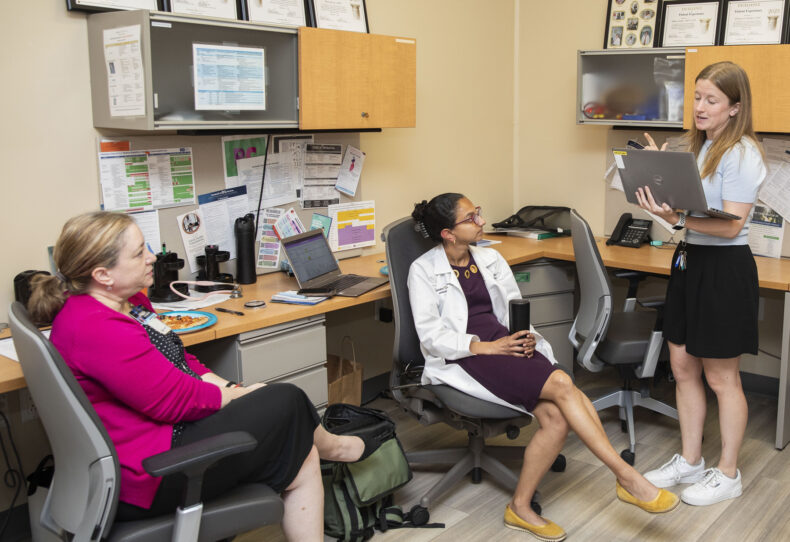 Medical student Callie Frey, co-executive director of Shade Tree Clinic, standing, discusses a patient's plan of care with, left to right, Tracy Hagemann, PharmD, and Rohini (Ro) Chakravarthy, MD, MBA, one of the clinic's medical directors. (photo by Susan Urmy) 