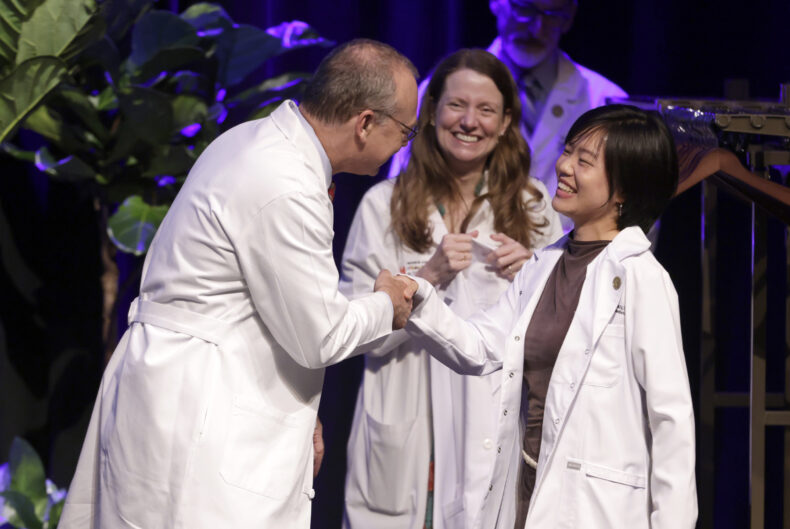 Wenqi “Jen” Zhao of Shanghai, China, shakes hands with Jeff Balser, MD, PhD, after receiving her white coat as Amy Fleming, MD, MHPE, looks on. (photo by Donn Jones)