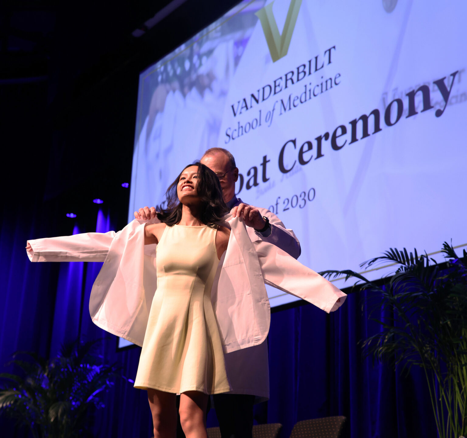 Jeff Balser, MD, PhD, helps Monica Zheng, a graduate of Harvard University, put on her white coat.