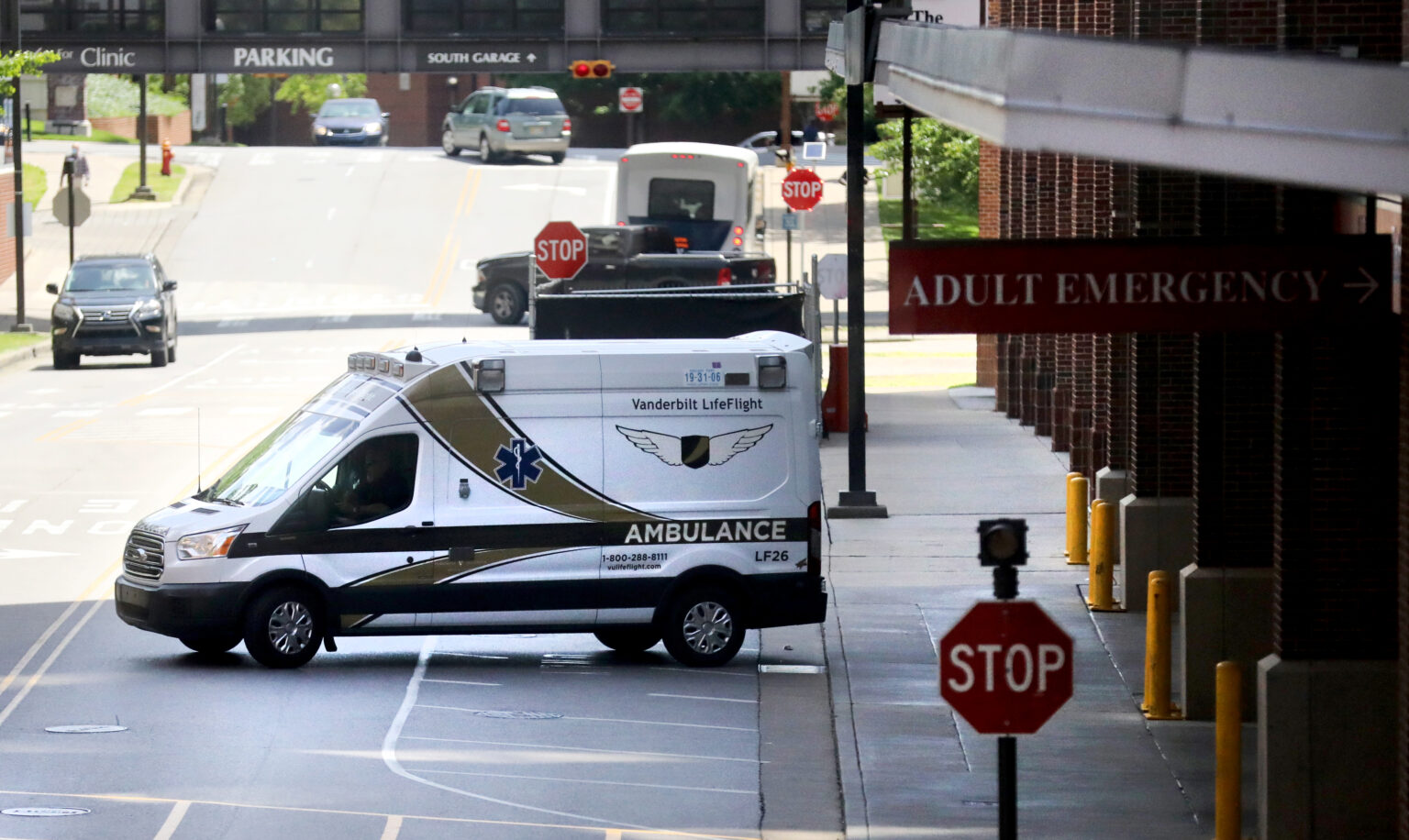 Vanderbilt LifeFlight ambulance on a hospital drive beside an “ADULT EMERGENCY” entrance sign, with stop signs, cars, a bus, and a parking garage in the background.