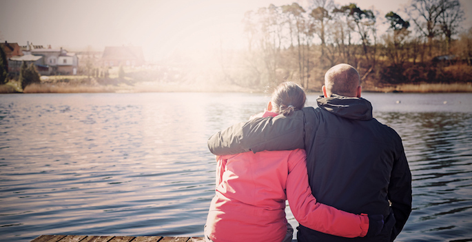 couple seated on a lake pier, photographed from behind